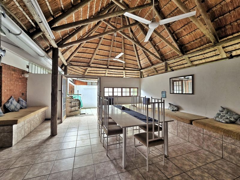 Spacious covered patio featuring a traditional thatched roof, exposed timber rafters, built-in bench seating, and tiled flooring, ideal for outdoor entertaining.