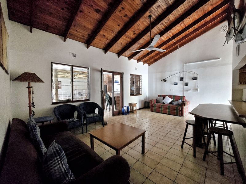 Spacious open-plan living and dining area featuring high exposed timber rafter ceilings, tiled flooring, and direct access to an outdoor patio.