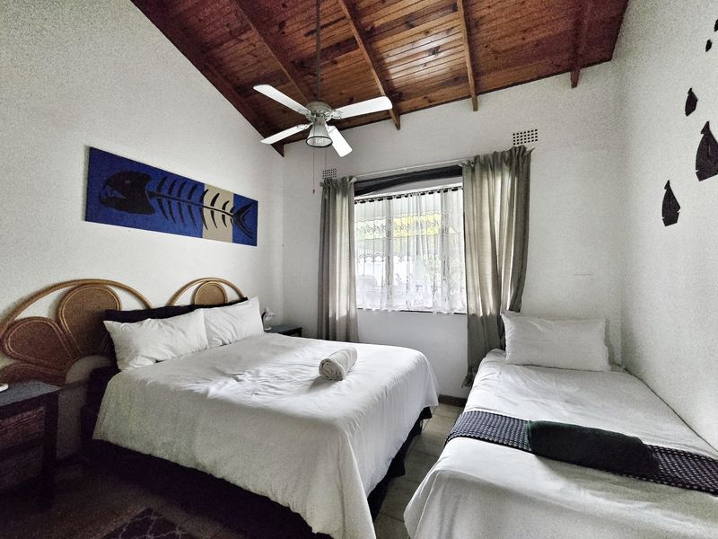 A bedroom featuring a high exposed timber rafter ceiling, ceiling fan, and natural light through a window.
