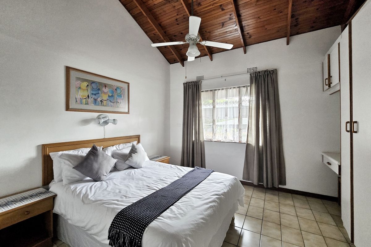 A bedroom featuring a vaulted timber ceiling, ceiling fan, tiled flooring, and built-in storage cupboards.