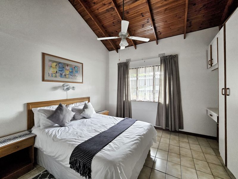 A bedroom featuring a vaulted timber ceiling, ceiling fan, tiled flooring, and built-in storage cupboards.