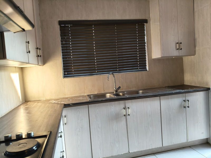 A functional kitchen featuring light wood-grain cabinetry, laminate countertops, a stainless steel double sink, and a built-in hob with an extractor fan.