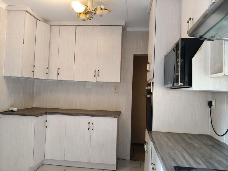 A functional kitchen featuring light-toned laminate cabinetry, dark countertops, built-in appliances, and tiled finishes throughout.