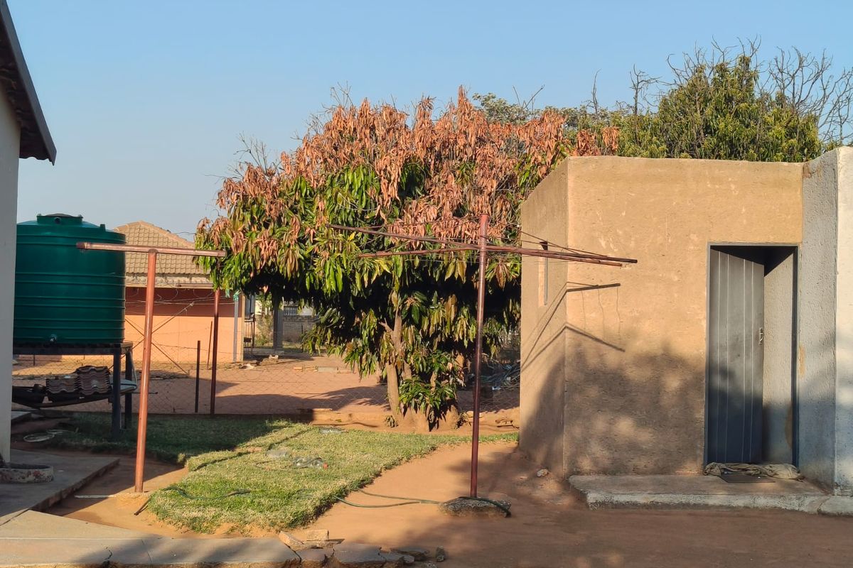 Rear yard area featuring a utility outbuilding, a water storage tank, and a metal washing line set within a simple garden space.