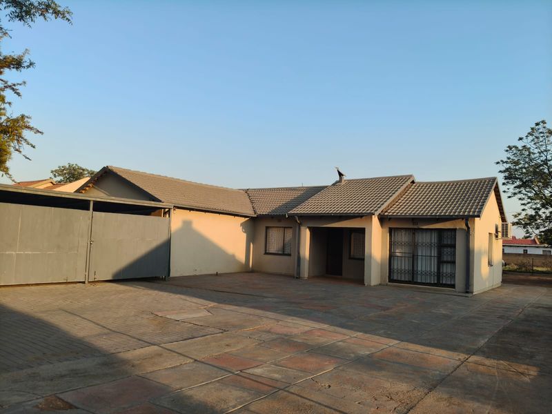 Front exterior view of a single-story house featuring a large paved driveway, tiled roof, and secure sliding door entrance.