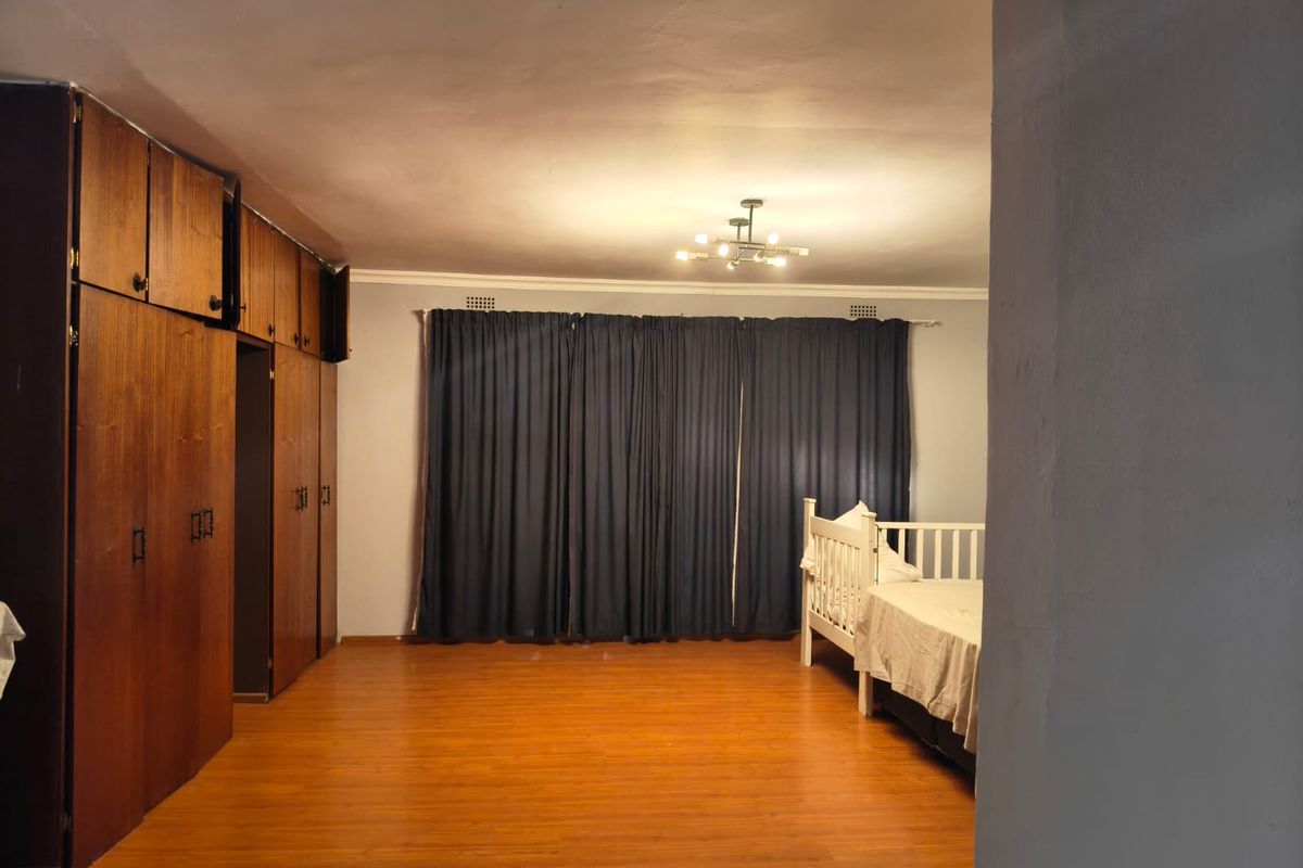 Spacious bedroom featuring extensive built-in wooden cabinetry, laminate flooring, and a central ceiling light fixture.