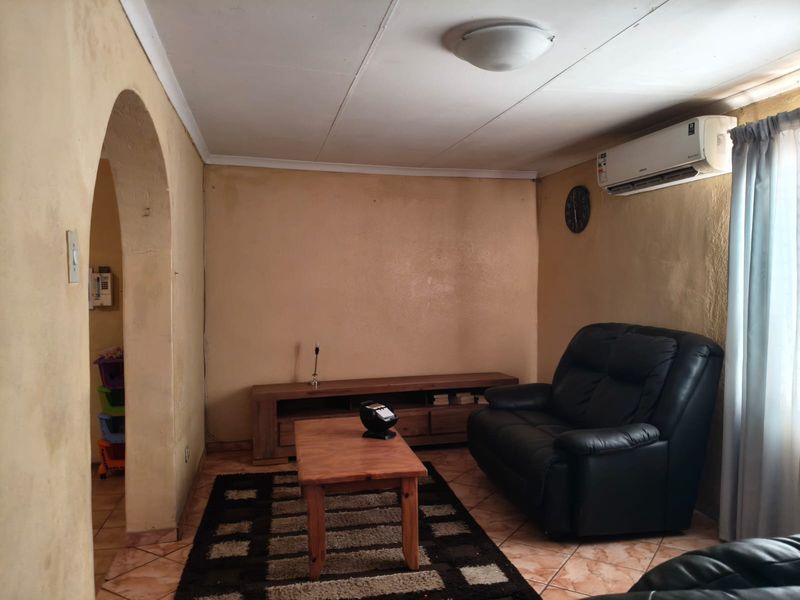 A living room featuring tiled flooring, an arched entryway, and a wall-mounted air conditioning unit, requiring cosmetic updates to the walls and ceiling.