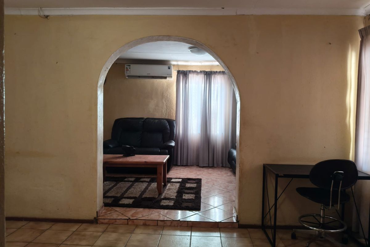 A living area featuring a distinctive arched doorway, tiled flooring, and a wall-mounted air conditioning unit, showing signs of wear on the wall finishes.