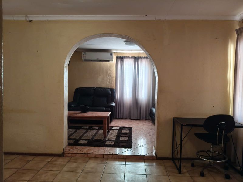 A living area featuring a distinctive arched doorway, tiled flooring, and a wall-mounted air conditioning unit, showing signs of wear on the wall finishes.