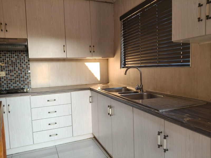 A functional kitchen featuring light wood-look cabinetry, a stainless steel double sink, mosaic tile backsplash, and built-in extractor fan.