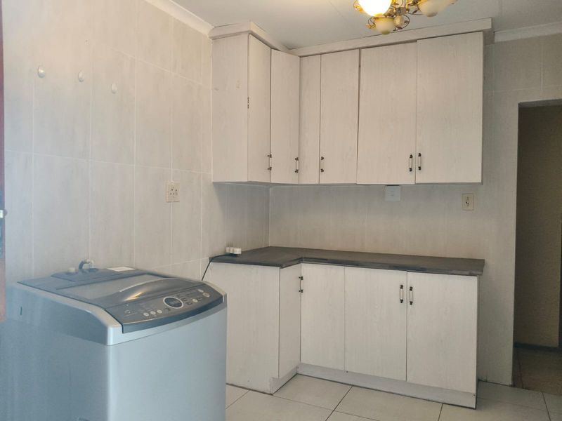 A functional laundry area featuring built-in white cabinetry, laminate countertops, and tiled wall and floor finishes.