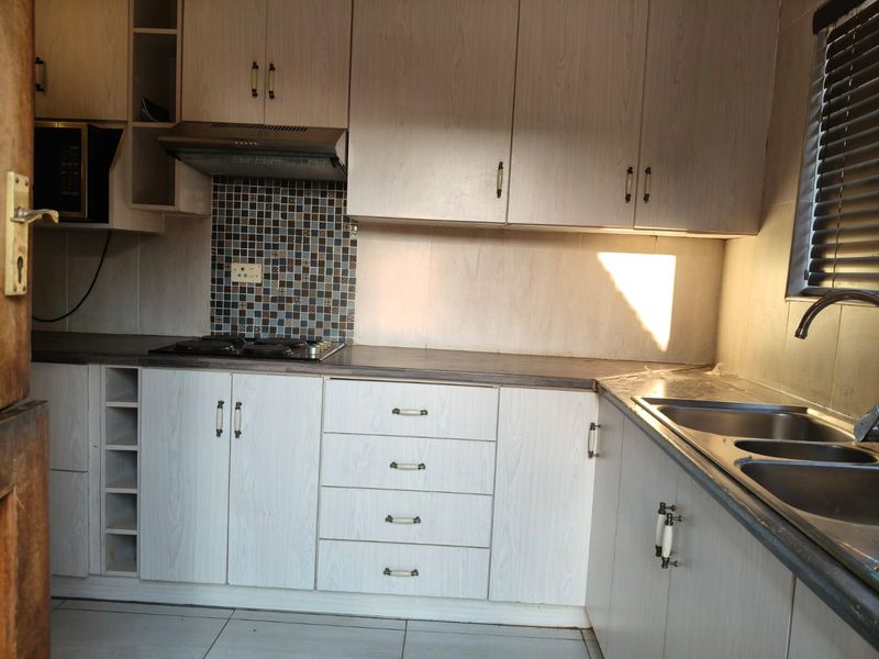 A functional kitchen featuring light wood-grain cabinetry, a mosaic tile backsplash, gas hob, extractor fan, and a stainless steel double sink.