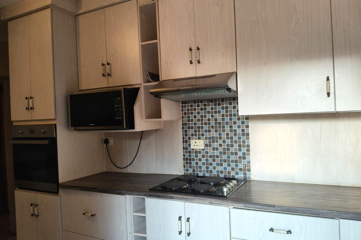 A functional kitchen featuring light wood-grain cabinetry, a dark laminate countertop, mosaic tile backsplash, and integrated appliances including an oven and electric hob.