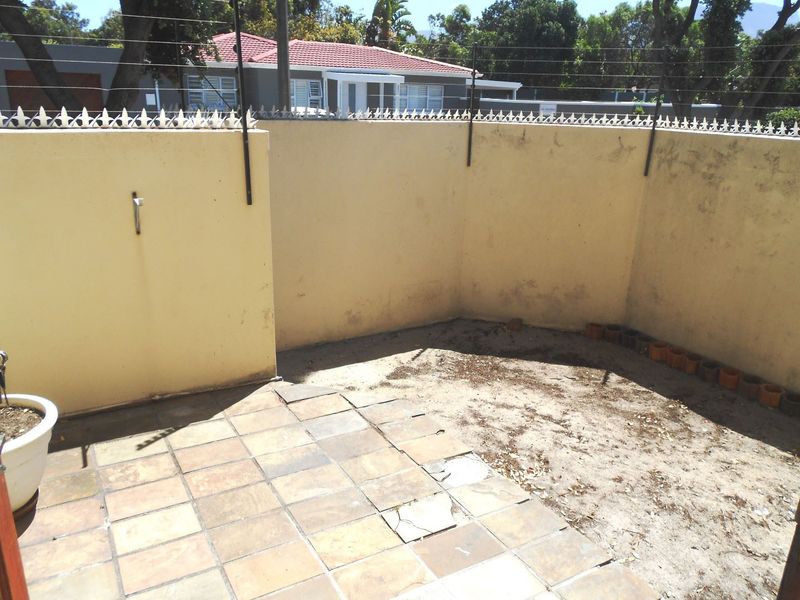 A rear courtyard area featuring a tiled patio section, perimeter wall with electric fencing, and an external water tap, requiring maintenance and landscaping.