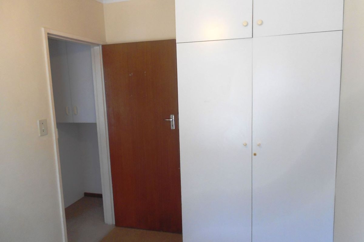 A bedroom featuring built-in white cupboards and a wooden internal door, providing functional storage space.