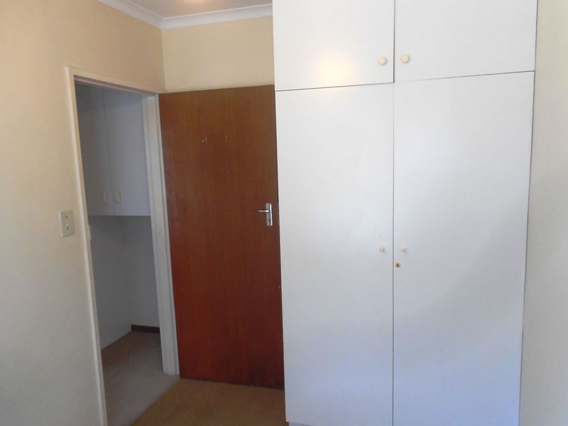 A bedroom featuring built-in white cupboards and a wooden internal door, providing functional storage space.