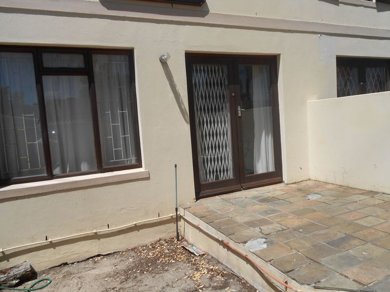 Rear exterior view of the townhouse featuring a tiled patio area, security gate, and double glass doors with aluminium window frames.