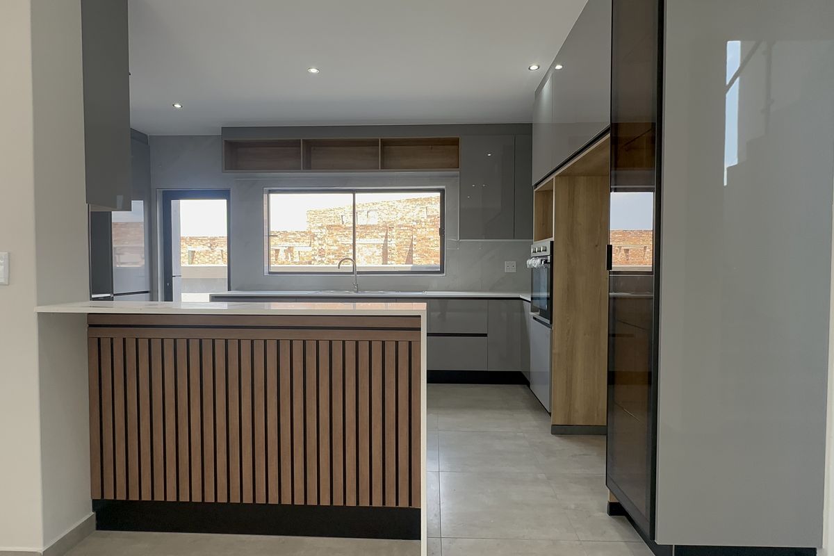 Modern kitchen featuring sleek grey cabinetry, timber accents, stone countertops, and a functional breakfast bar with integrated oven and recessed lighting.