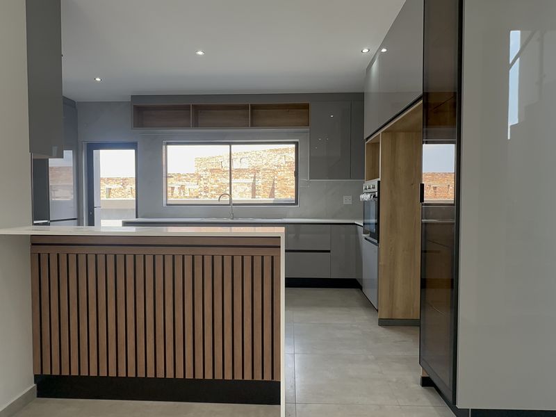 Modern kitchen featuring sleek grey cabinetry, timber accents, stone countertops, and a functional breakfast bar with integrated oven and recessed lighting.