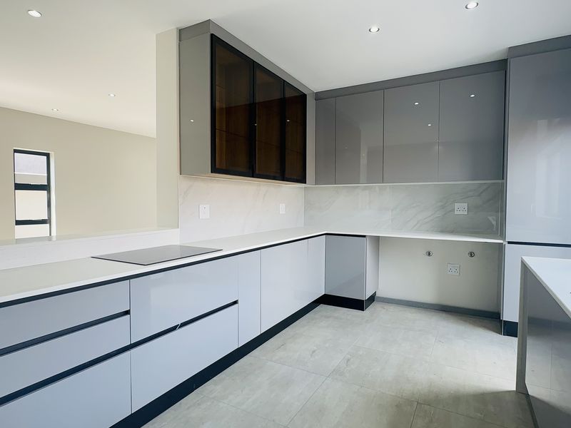 Modern, minimalist kitchen featuring sleek grey cabinetry, stone countertops, marble-look splashbacks, and integrated hob, offering a clean and contemporary culinary space.