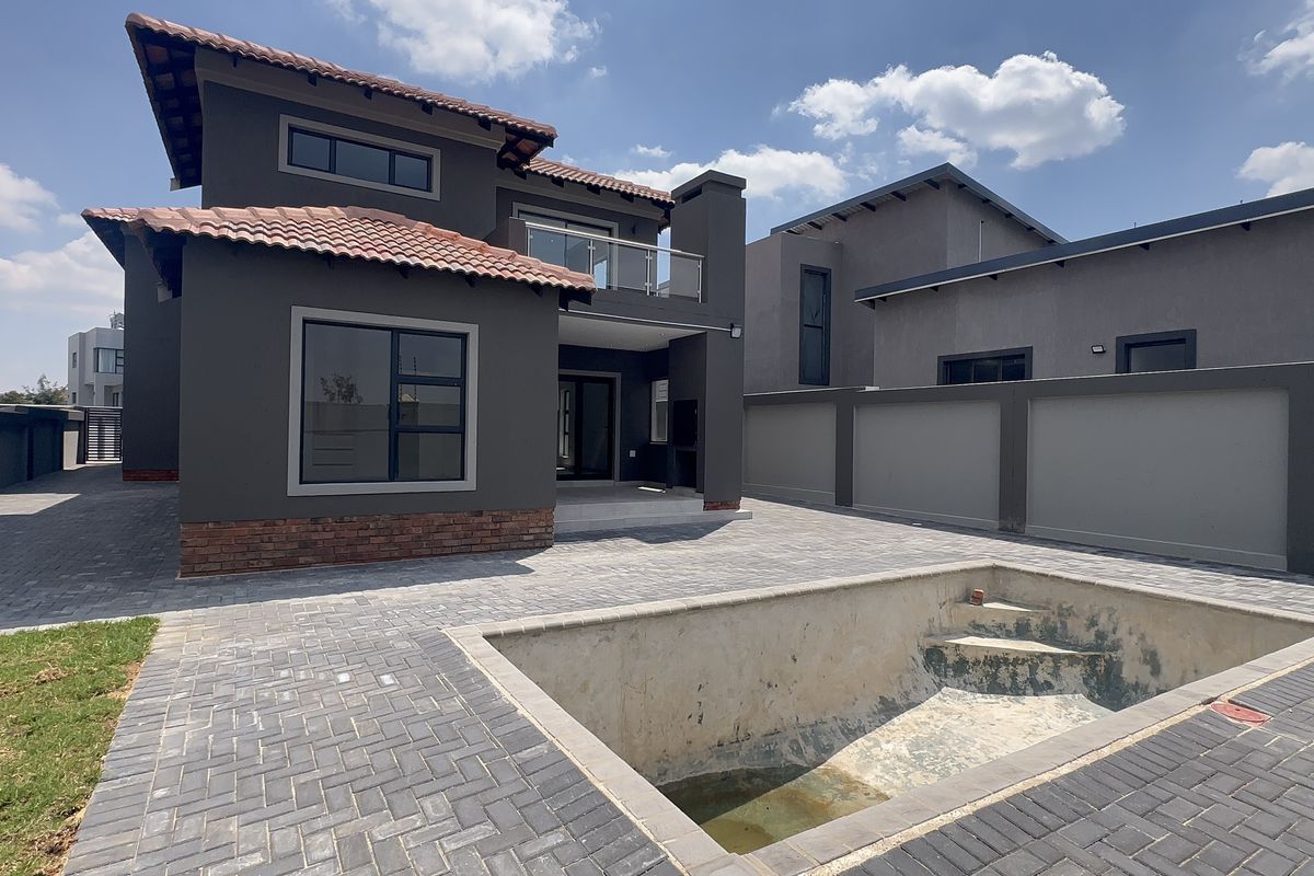 Rear exterior view of a modern two-story house featuring a paved patio, balcony, and an empty swimming pool requiring maintenance.