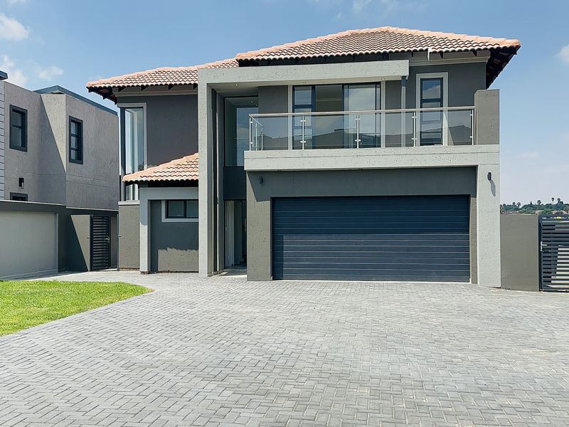Modern double-story residential home featuring a tiled roof, integrated double garage, paved driveway, and an upper-level balcony with glass balustrades.