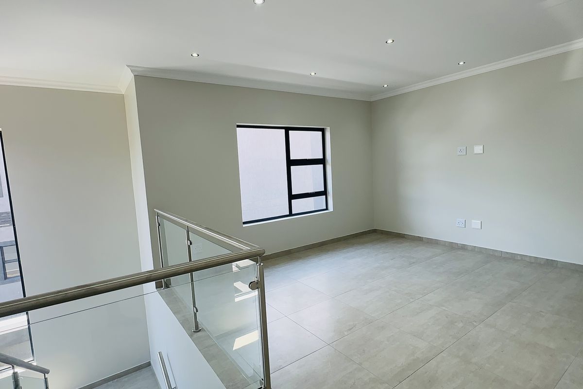 A bright, modern, and empty living area featuring neutral tiled flooring, recessed downlighting, and a contemporary glass balustrade overlooking the lower level.
