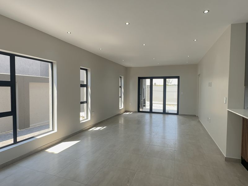 Spacious open-plan living area featuring modern porcelain floor tiles, recessed downlighting, and large aluminium sliding doors leading to the exterior.