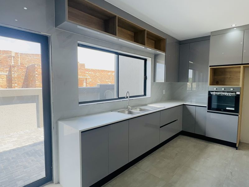 Modern kitchen featuring sleek grey cabinetry, quartz countertops, built-in oven, and direct access to an outdoor patio area.