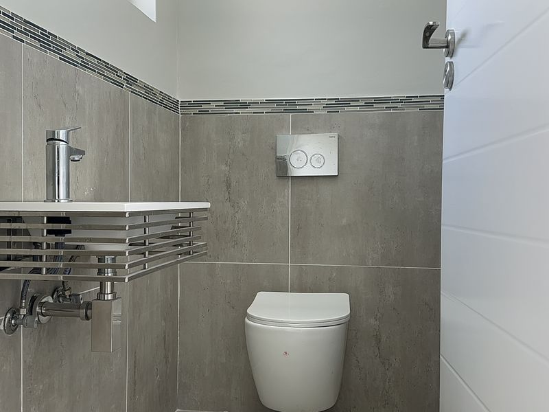 A modern guest bathroom featuring a wall-mounted toilet with a concealed cistern and a contemporary wall-mounted basin with chrome fixtures.