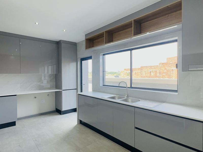 Modern kitchen featuring sleek grey cabinetry, stone countertops, a double sink, and marble-look splashbacks, offering a clean and contemporary aesthetic.
