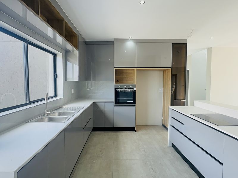 Modern kitchen featuring sleek grey gloss cabinetry, stone countertops, integrated oven, induction hob, and a double sink with contemporary finishes.