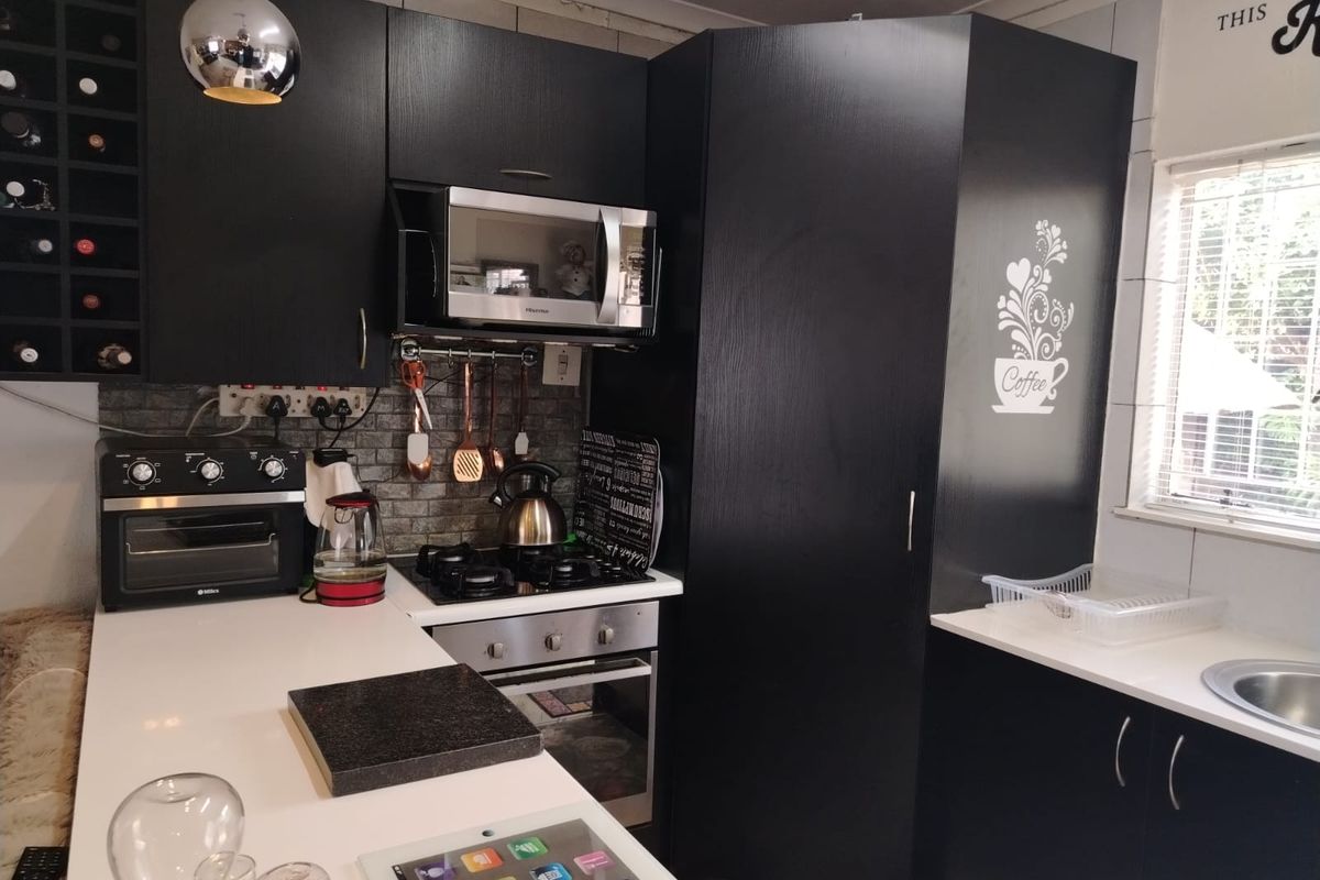 Modern kitchen featuring black cabinetry, stone countertops, built-in gas hob, oven, and integrated microwave with a tiled backsplash and wine storage.