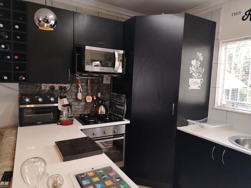 Modern kitchen featuring black cabinetry, stone countertops, built-in gas hob, oven, and integrated microwave with a tiled backsplash and wine storage.
