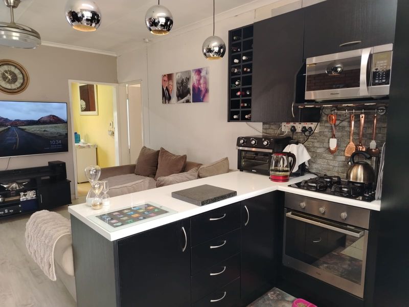 Open-plan living area featuring a modern kitchen with dark cabinetry, stone countertops, built-in oven, gas hob, and integrated microwave, flowing into the lounge space.