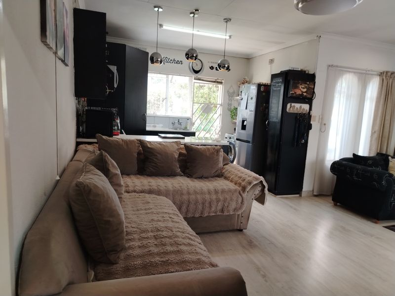Open-plan living area featuring a functional kitchen with dark cabinetry, pendant lighting, and light-toned laminate flooring, creating a connected and versatile living space.
