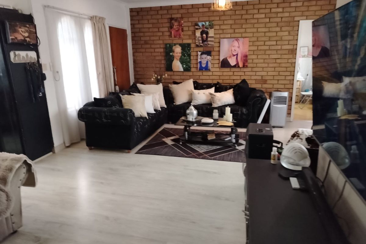 Spacious living room featuring a prominent exposed brick feature wall and light-toned laminate flooring, offering a comfortable and versatile living space.