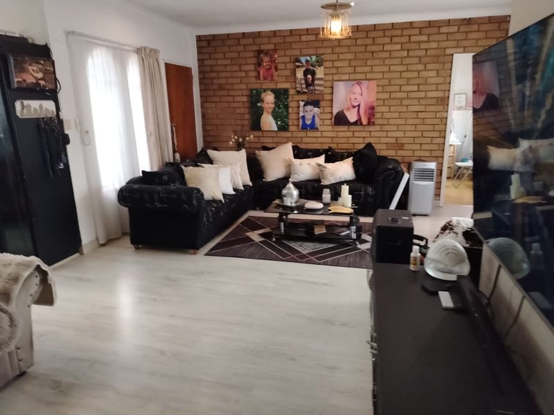 Spacious living room featuring a prominent exposed brick feature wall and light-toned laminate flooring, offering a comfortable and versatile living space.