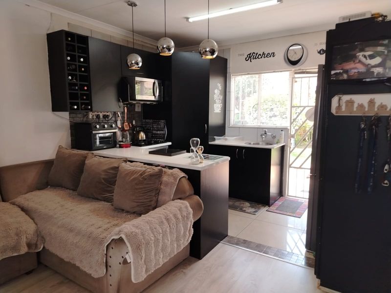 Open plan living and kitchen area featuring dark cabinetry, contrasting countertops, and a mix of tiled and laminate flooring with direct access to the exterior.