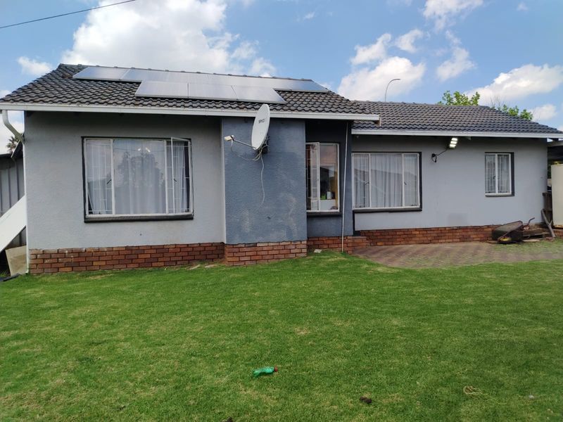 Rear view of a single-story house featuring a tiled roof with solar panels, brick base detailing, security bars on windows, and a paved patio area.