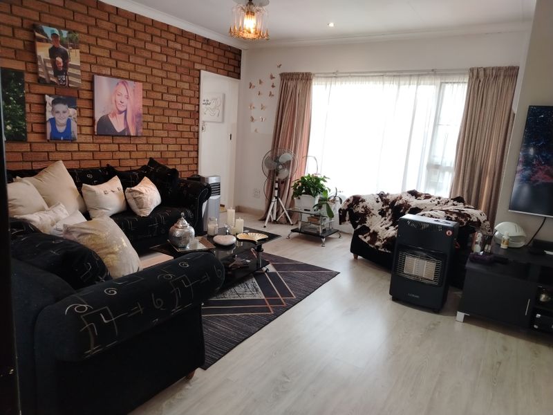 A living room featuring a prominent exposed brick wall, light-toned laminate flooring, and large windows with curtains, providing a warm and textured living space.