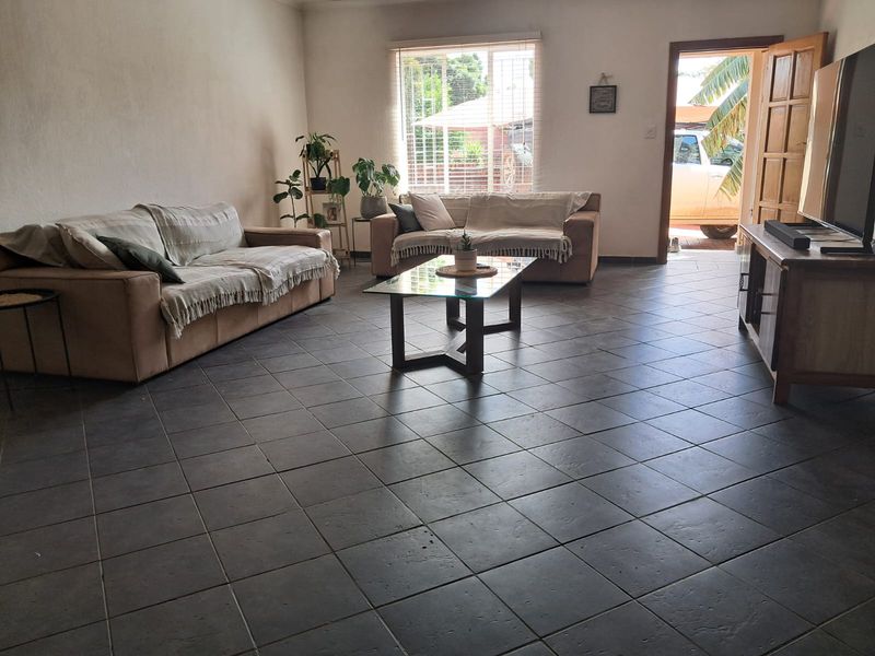 Spacious living room featuring dark tiled flooring, natural light from a large window, and direct access to the exterior.