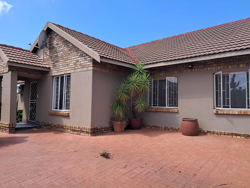 A well-maintained single-story house featuring a brick-paved driveway, tiled roof, and secure window bars, presenting a neat and tidy front facade.
