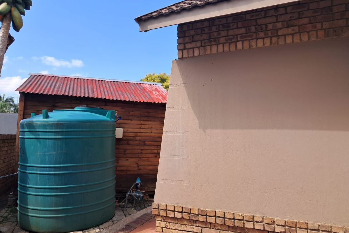 Rear exterior view showing a brick house wall, a large water storage tank, and a timber shed with a corrugated metal roof.