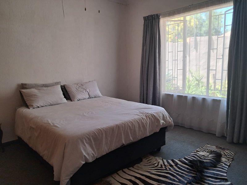 A bedroom featuring carpeted flooring and a large window with security bars, requiring cosmetic updates to the wall finishes.