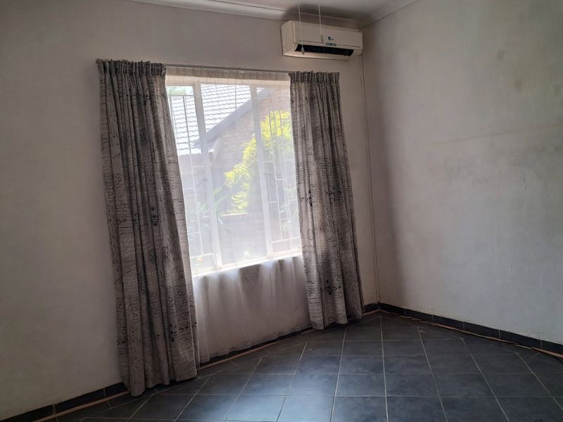 An empty bedroom featuring tiled flooring, a wall-mounted air conditioning unit, and a window with security bars.