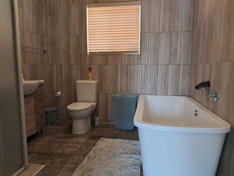 Modern bathroom featuring a freestanding bathtub, vanity cabinet with basin, toilet, and neutral floor-to-ceiling wall tiling.