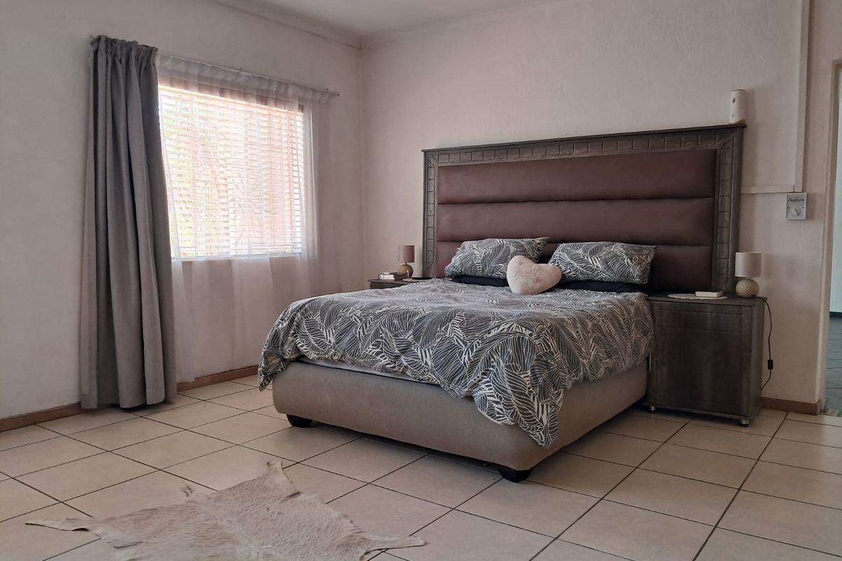 A spacious bedroom featuring neutral tiled flooring, recessed lighting, and a large window with fitted blinds.