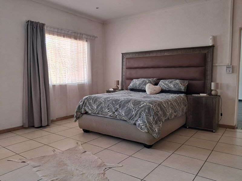 A spacious bedroom featuring neutral tiled flooring, recessed lighting, and a large window with fitted blinds.
