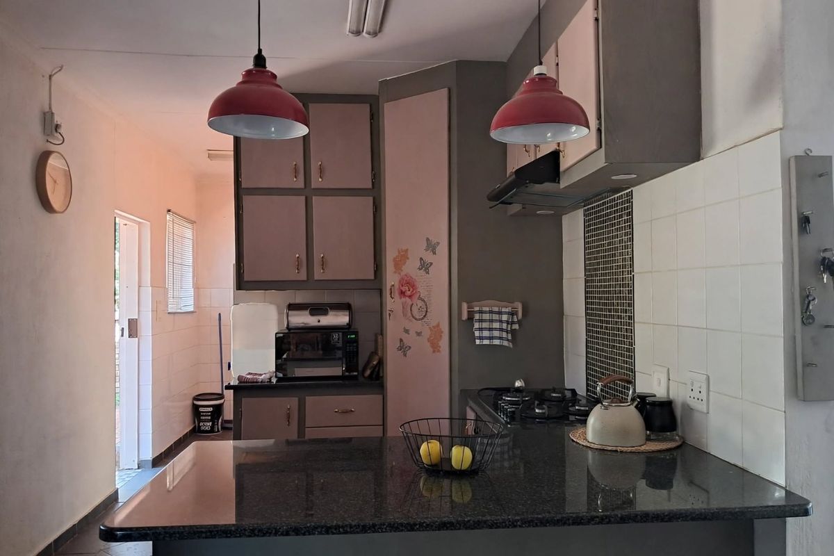 A functional kitchen featuring granite countertops, built-in cabinetry, a gas hob with extractor fan, and tiled backsplash, offering a practical layout for daily use.